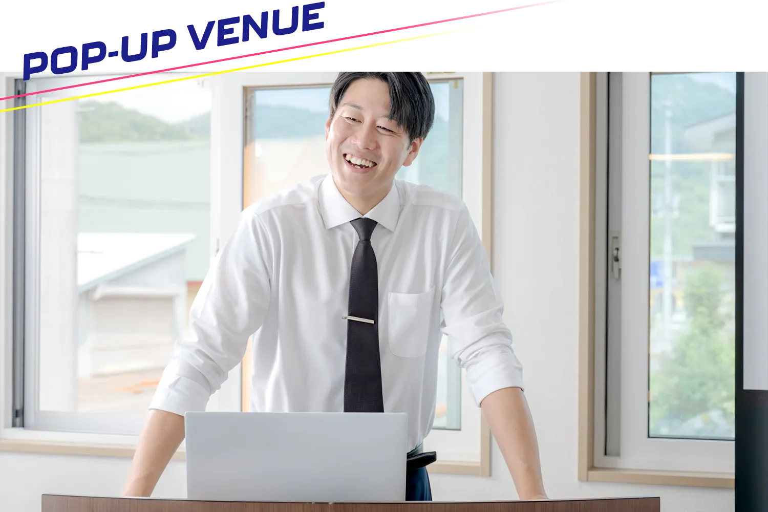 演台にノート型パソコンを置いて話す男性の写真